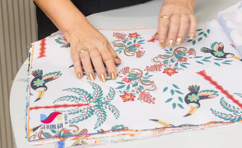 Mãos conferindo tecido estampado com tucanos
